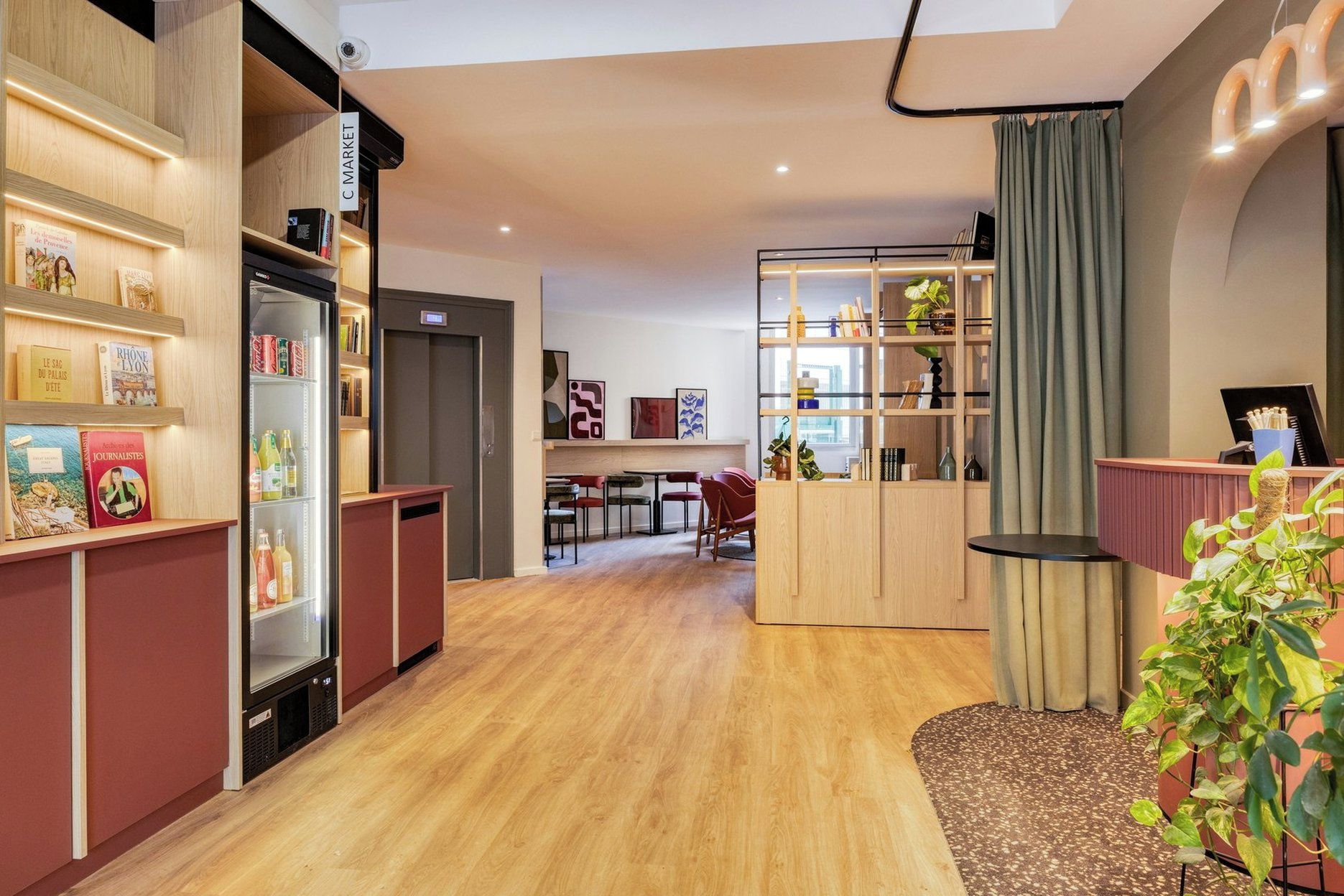 A modern interior with a kitchen area, wooden shelves with books and bottles, and a dining space with chairs and tables.