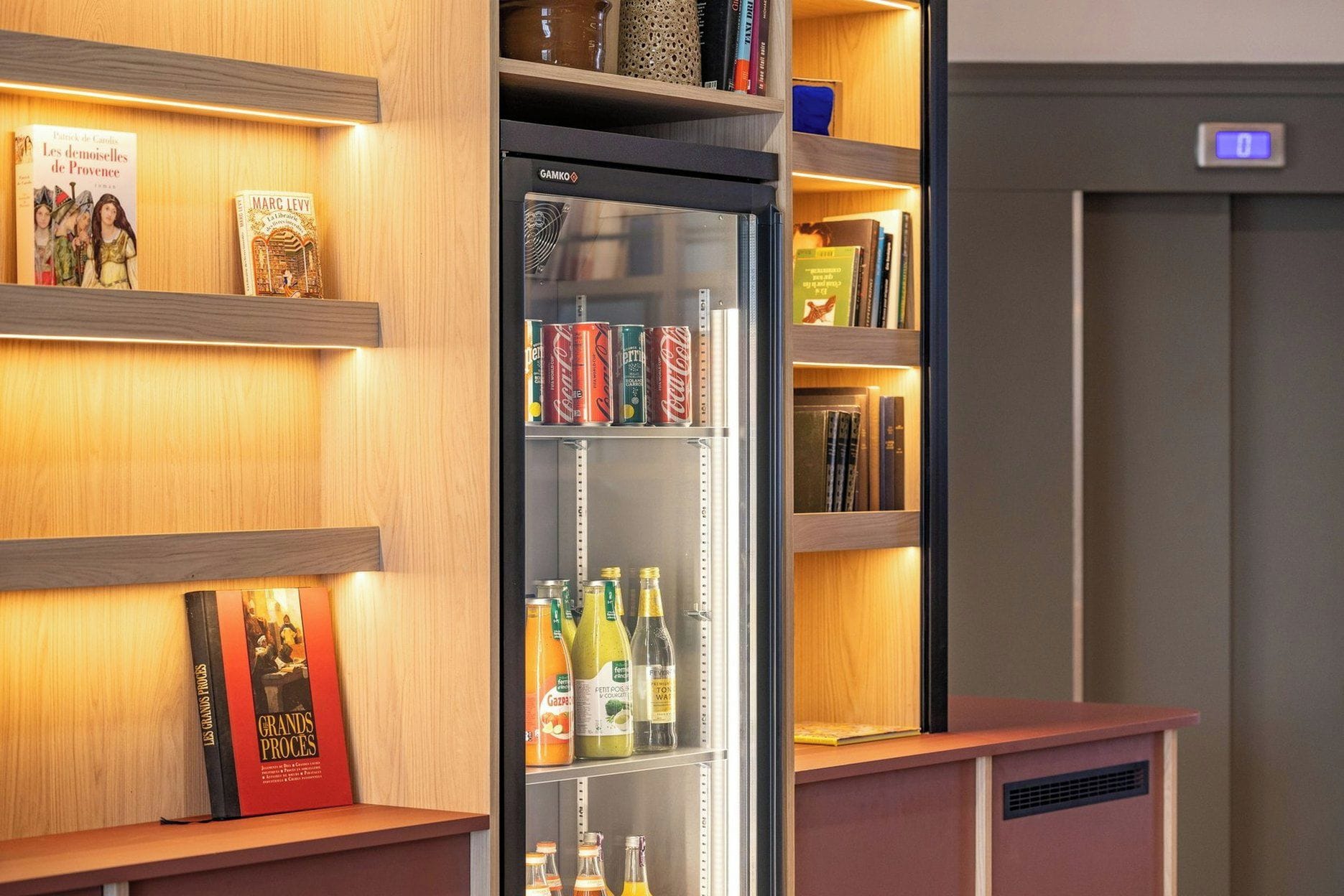 A hotel room with a minibar, bookshelves, and a refrigerator stocked with beverages.