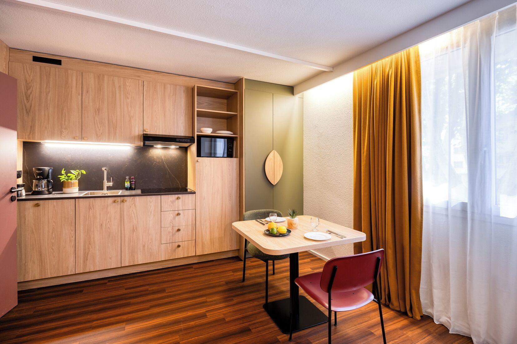 A compact kitchen with wooden cabinets, a microwave, and a dining area with a table and chairs.