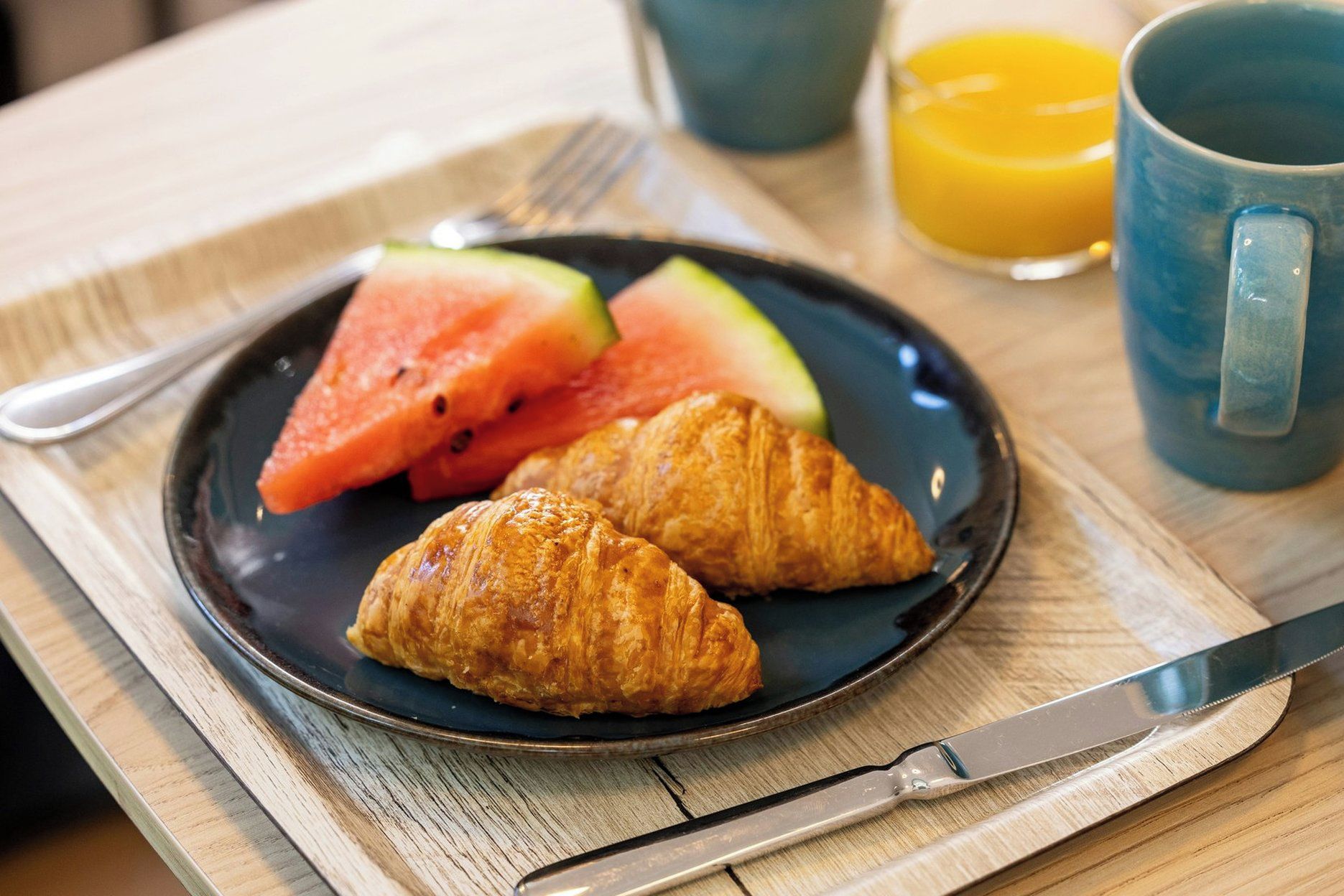 Ein Frühstücksbrett mit Croissants, Wassermelone und einem Glas Orangensaft.
