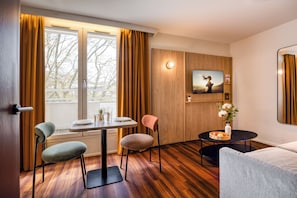 A modern room with a wooden floor, a dining table with chairs, a sofa, a TV mounted on the wall, and a small table with a vase of flowers. - Citadines Part-Dieu Lyon (Lyon)