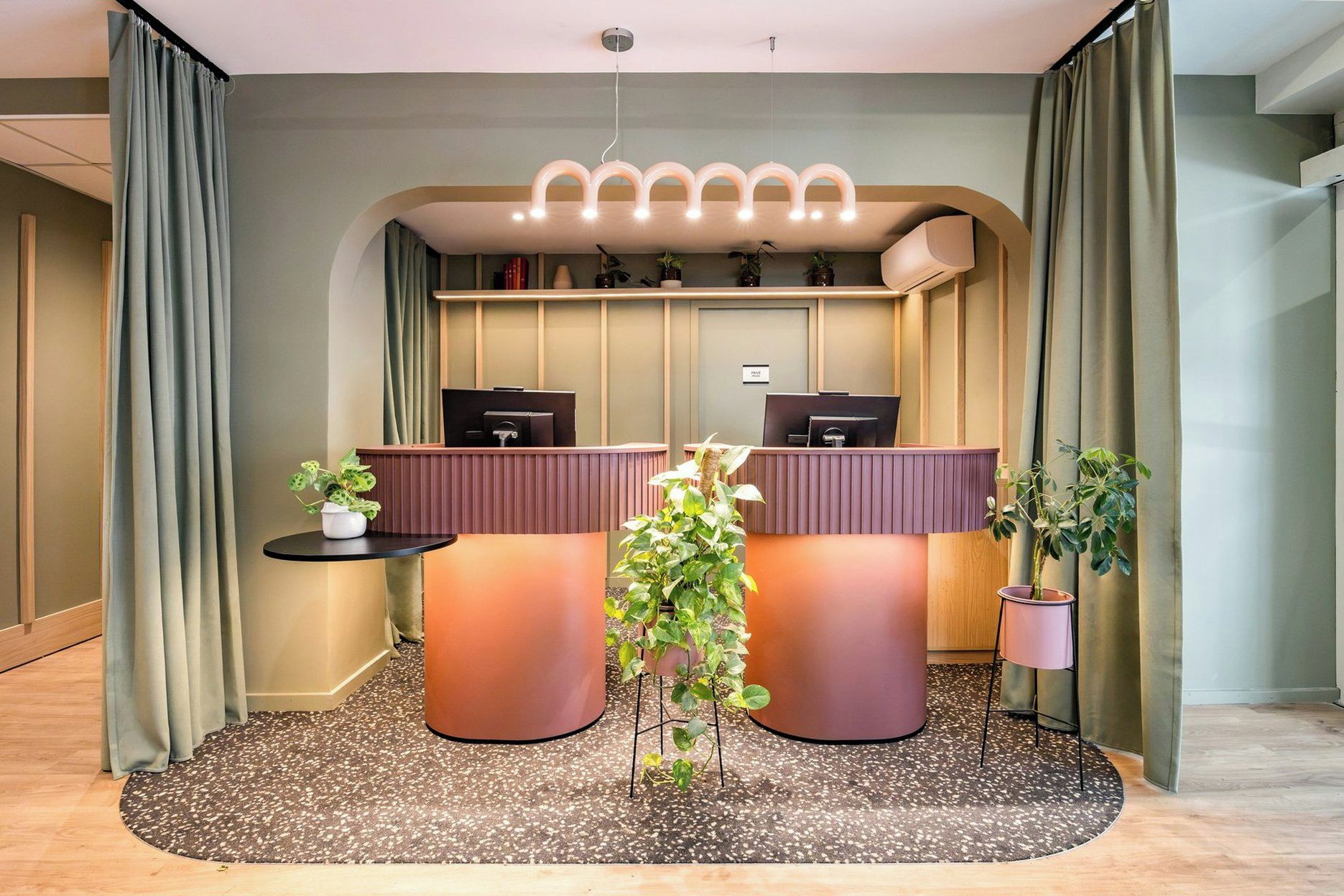 Un espace d’accueil comprenant deux comptoirs, une petite table avec une plante et un luminaire décoratif suspendu au plafond.