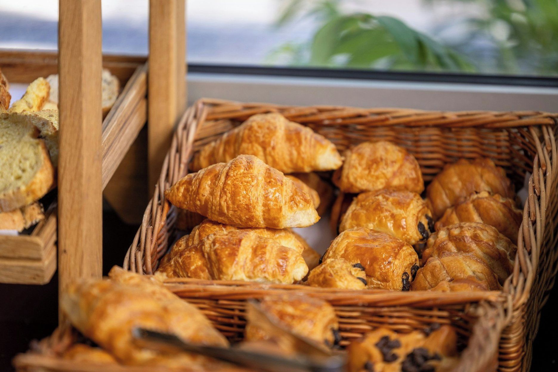 A basket of assorted pastries, including croissants and bread, displayed in a wicker basket.