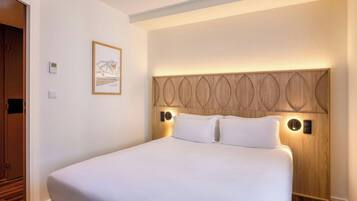 A hotel room with a large bed, a headboard with a unique design, and a wall-mounted light fixture.