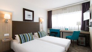 Hotelkamer met twee bedden, een bureau, een stoel, een televisie en een raam met gordijnen.
