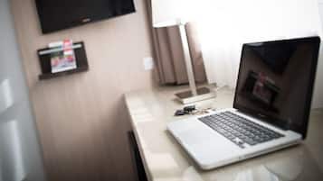 Een hotelkamer met een laptop op een bureau, een aan de muur bevestigde televisie en een lamp.