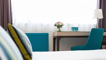 Habitación de hotel con cama, escritorio con silla, lámpara y ventana con cortinas.