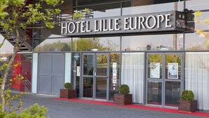 Het uiterlijk van Hotel Lille Europe met grote glazen deuren, een rode loper en twee potplanten.