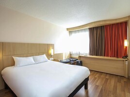 Una habitación de hotel con una cama grande, un escritorio con lámpara y una ventana con cortinas.