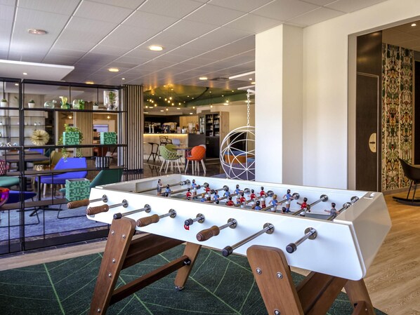 Una mesa de fútbol de mesa en un ambiente interior moderno, con un área de comedor al fondo.