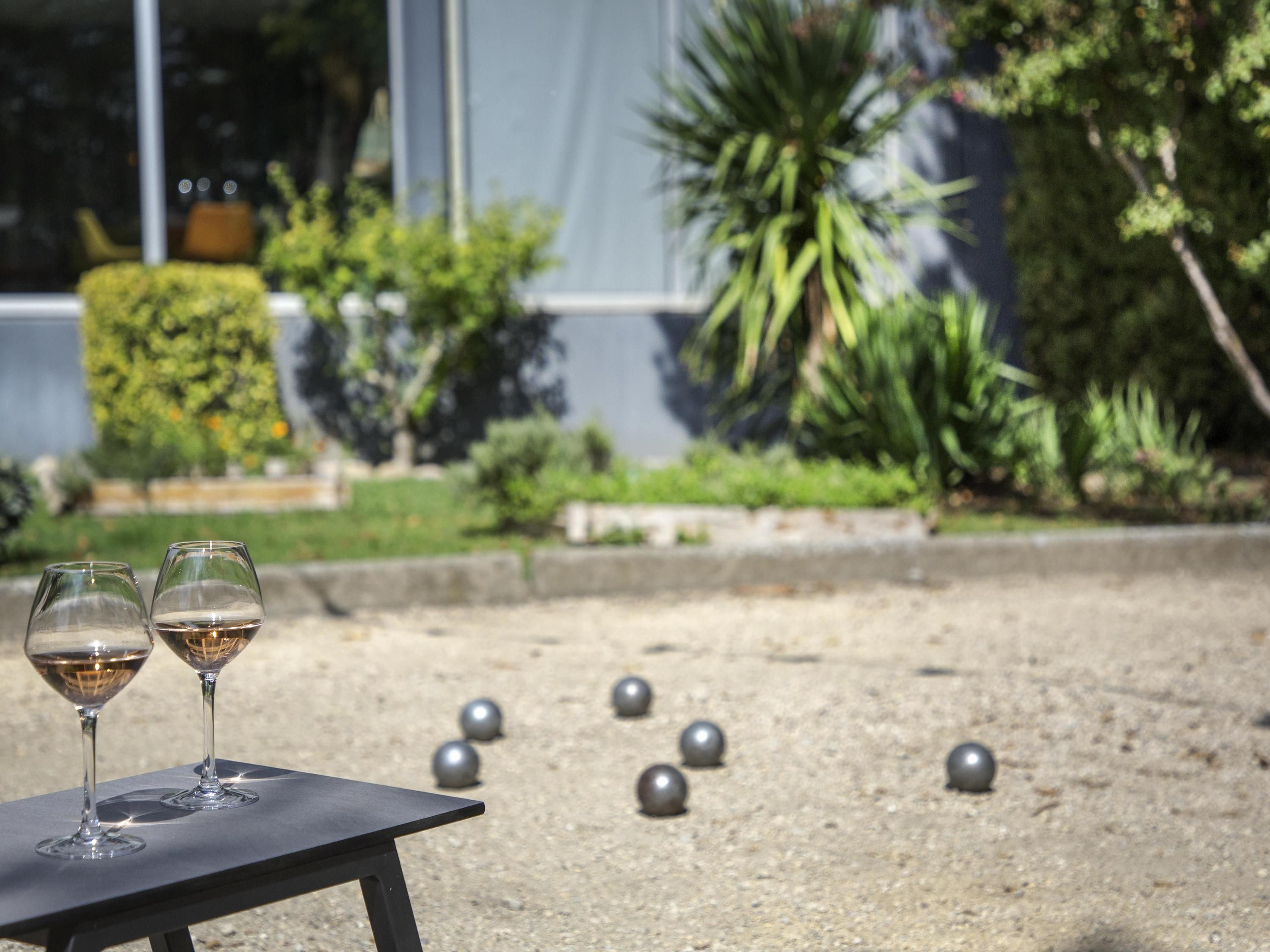 Dos copas de vino sobre una mesa, con un jardín y un edificio al fondo.