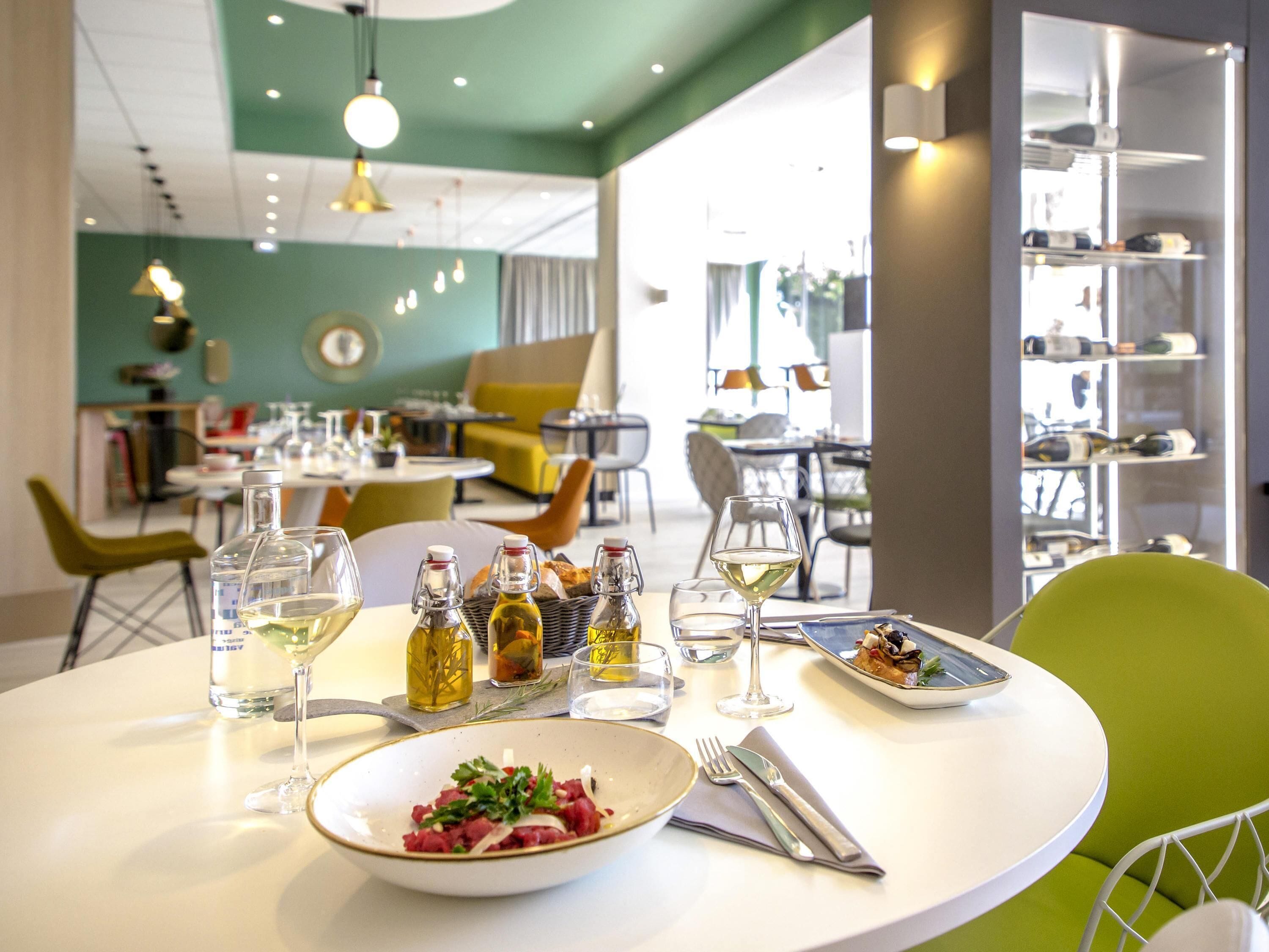 A dining area with tables set for meals, bottles of olive oil, and glasses of white wine.