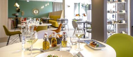 A dining area with tables set for meals, bottles of olive oil, and glasses of white wine.
