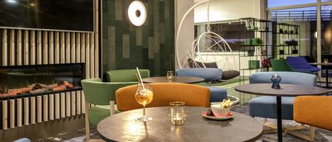 Un espace de détente moderne avec des tables rondes, des sièges confortables, une cheminée et un grand écran de télévision.