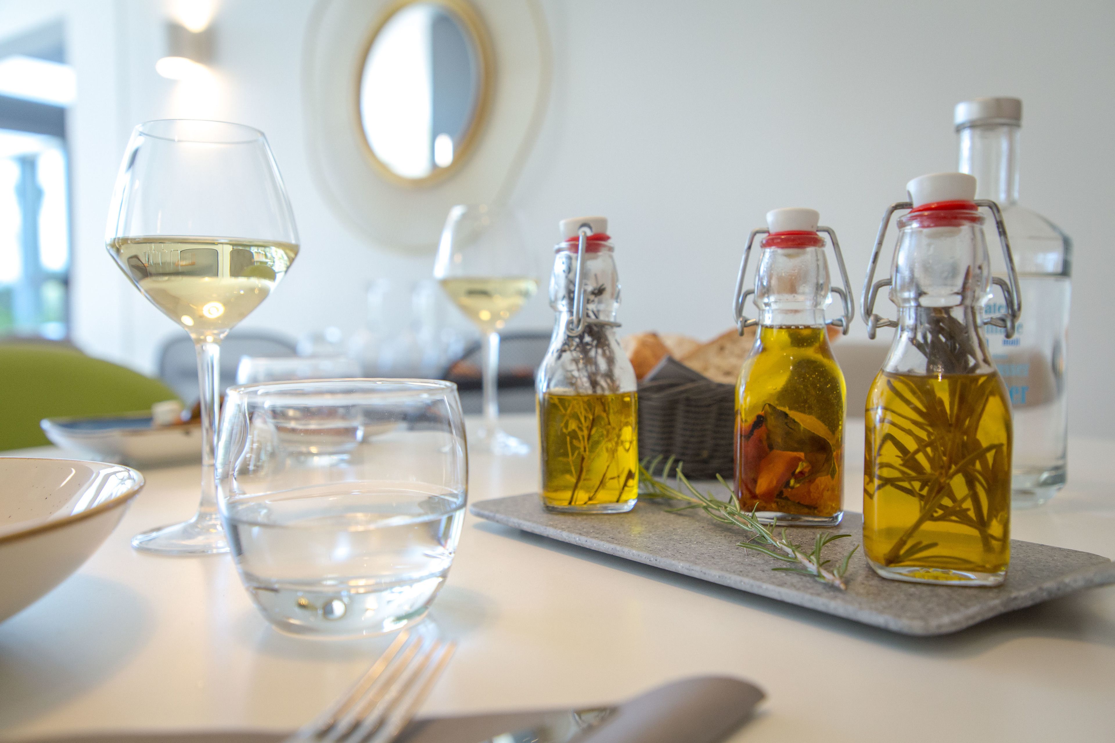 A table with a glass of white wine, two bottles of olive oil, and a glass of water.