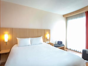 A hotel room with a large bed, two bedside lamps, a chair, a desk, and a suitcase.