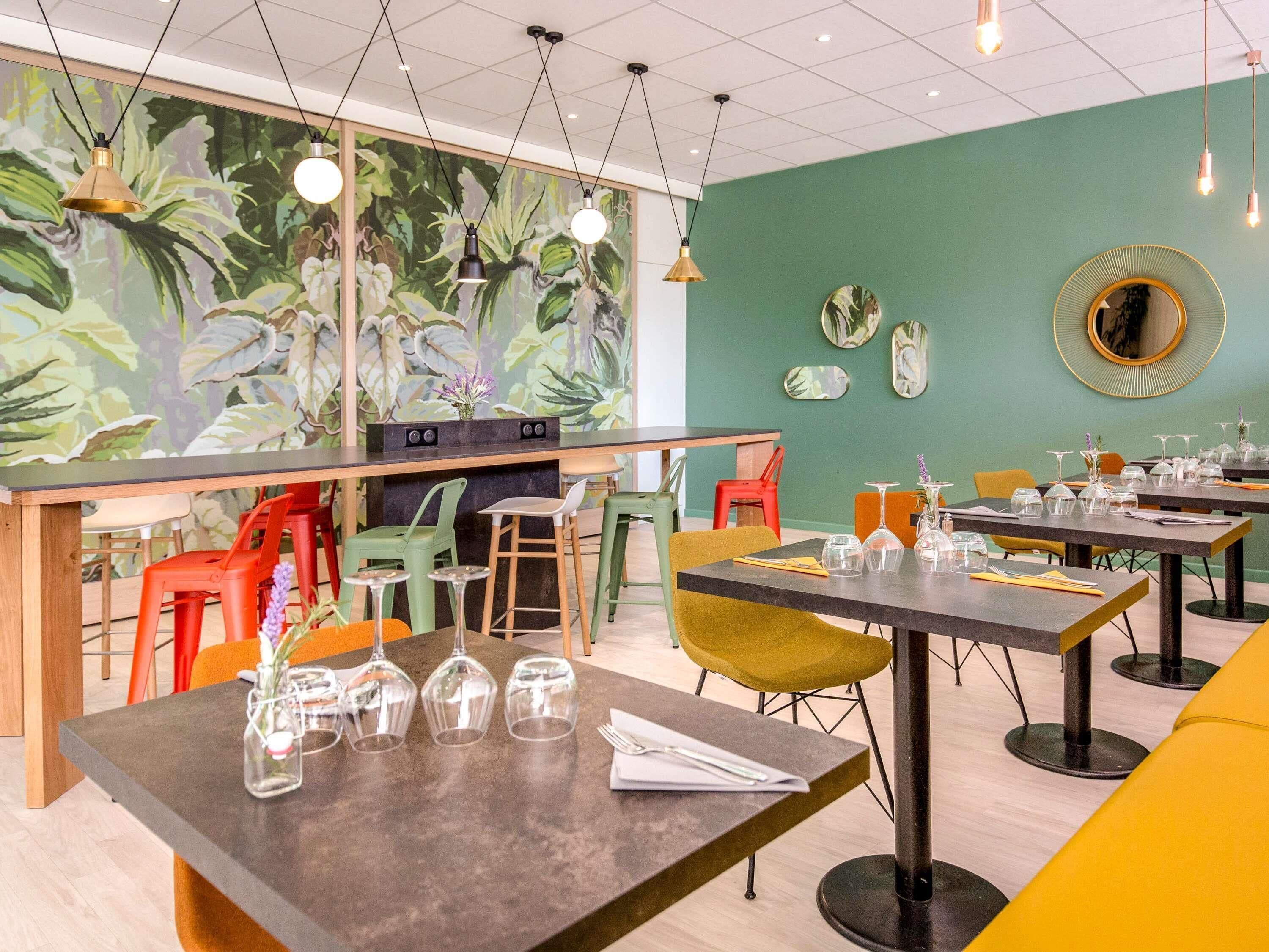 A restaurant interior with tables, chairs, and a mural of foliage on the wall.