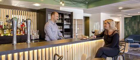 Zona de bar con mostrador, taburetes y estanterías llenas de botellas.