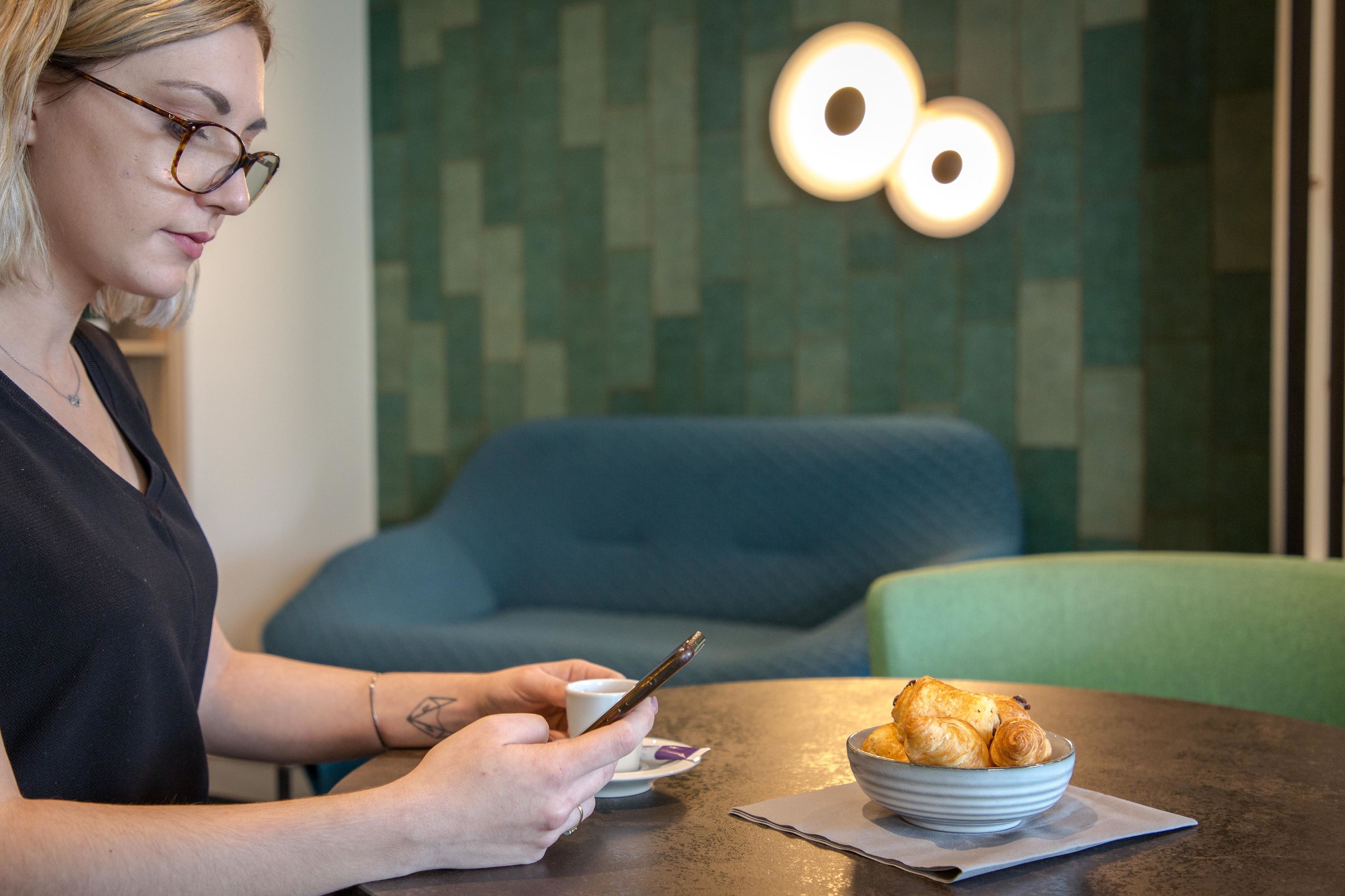 Una persona sentada a una mesa con un bol de cruasanes y una taza, en una habitación de diseño moderno y una silla azul al fondo.