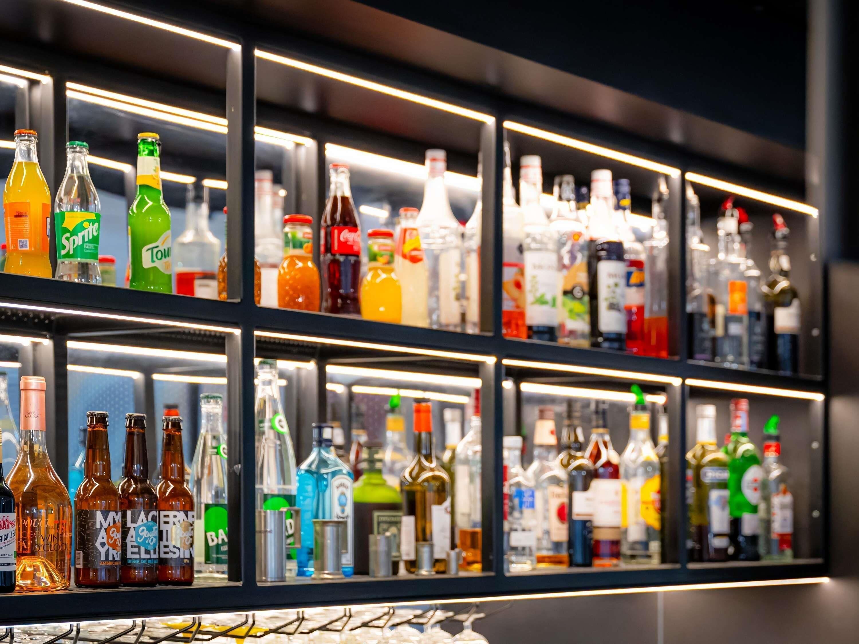 Un bar con estantes llenos de botellas variadas, incluyendo licores y refrescos.