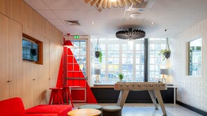 A modern interior with a red sofa, a foosball table, and a staircase. - ibis Paris Ornano Montmartre Nord 18ème (Paris)