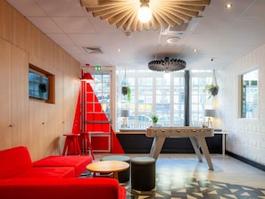 A modern interior with a red sofa, a foosball table, and a staircase. - ibis Paris Ornano Montmartre Nord 18ème (Paris)
