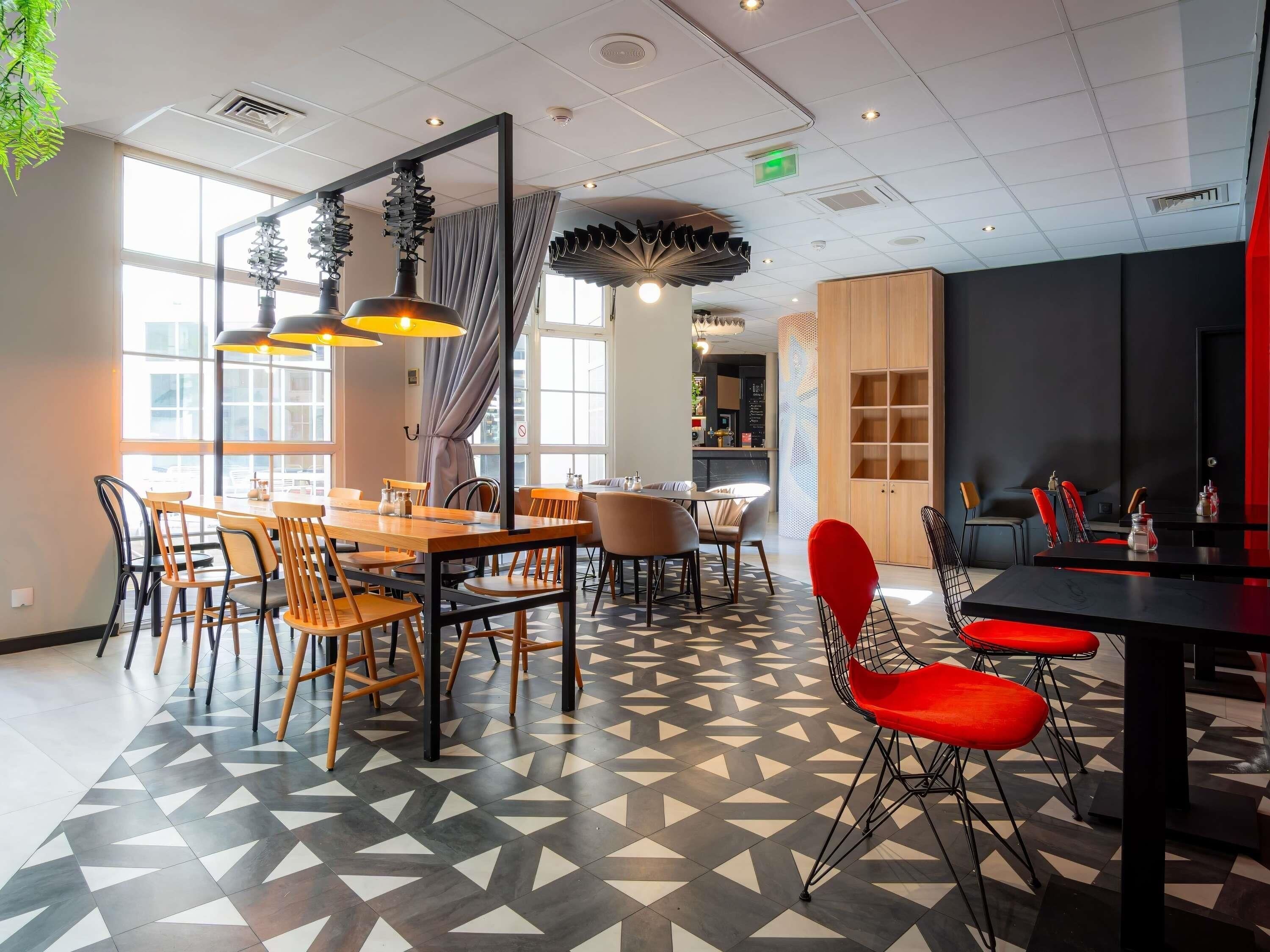Zona pranzo moderna con pavimento a motivi geometrici, tavoli in legno e sedie rosse.
