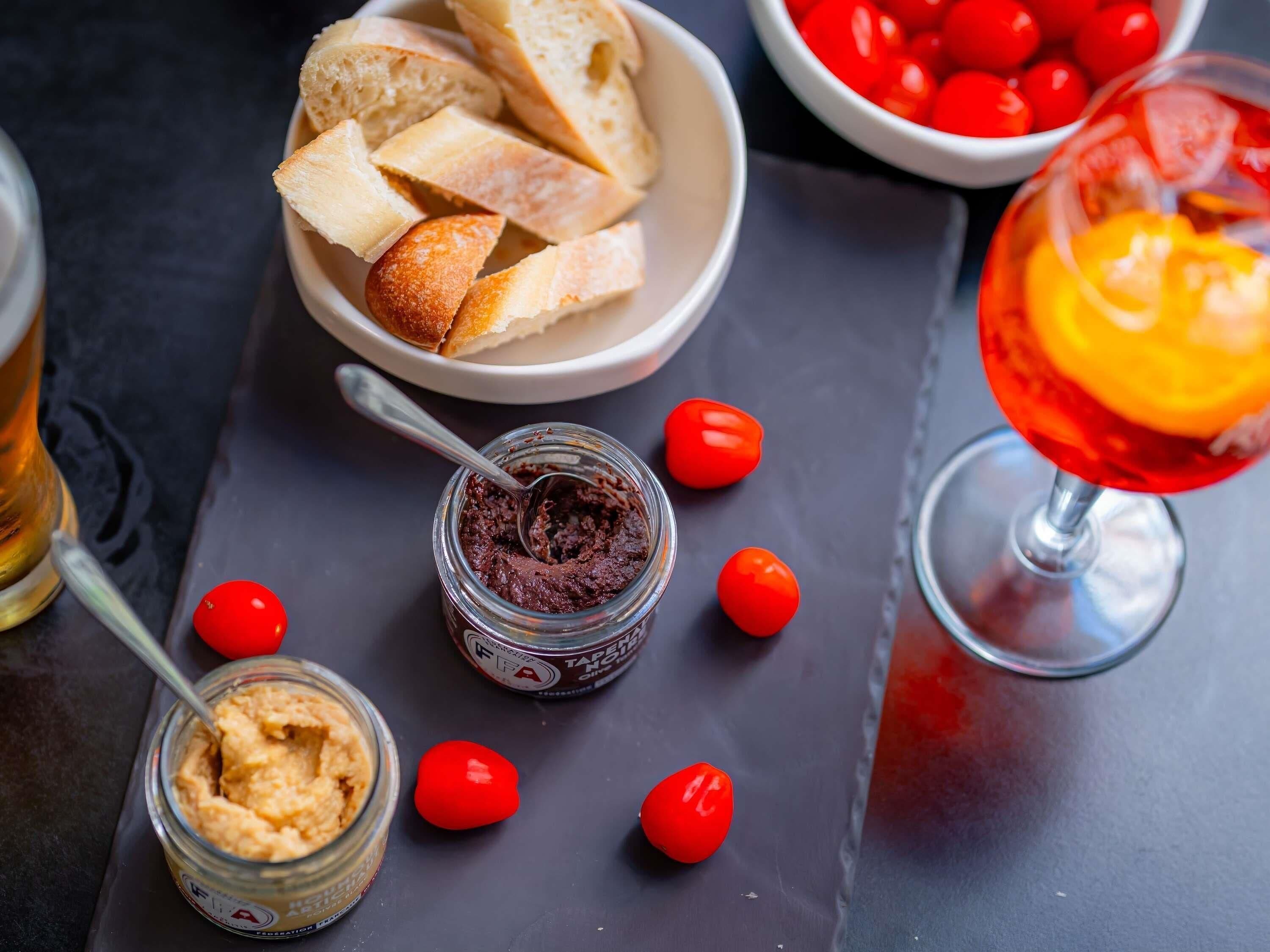 Een tafel met brood, tomaten, een potje beleg en een glas drinken.
