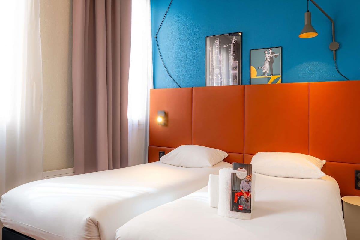 Ein Hotelzimmer mit zwei Betten, einer blauen Akzentwand, einem gerahmten Bild und einer Lampe.