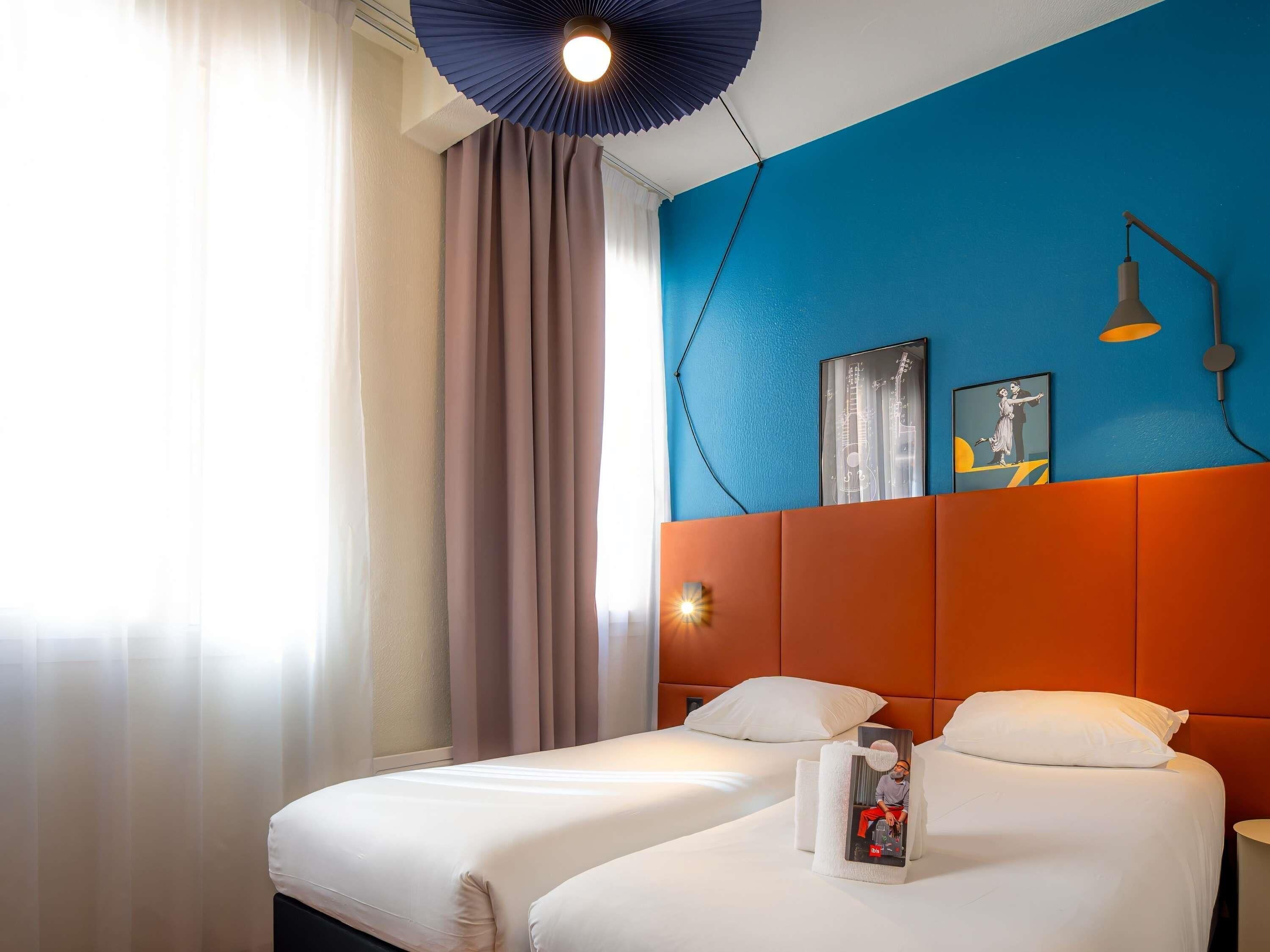 A hotel room with two beds, a blue accent wall, a ceiling light, and a framed picture.