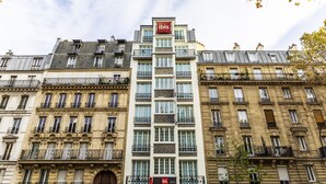 A multi-story hotel with a prominent 'ibis' sign, featuring a classic architectural style with ornate balconies and large windows. - ibis Paris Ornano Montmartre Nord 18ème (Paris)