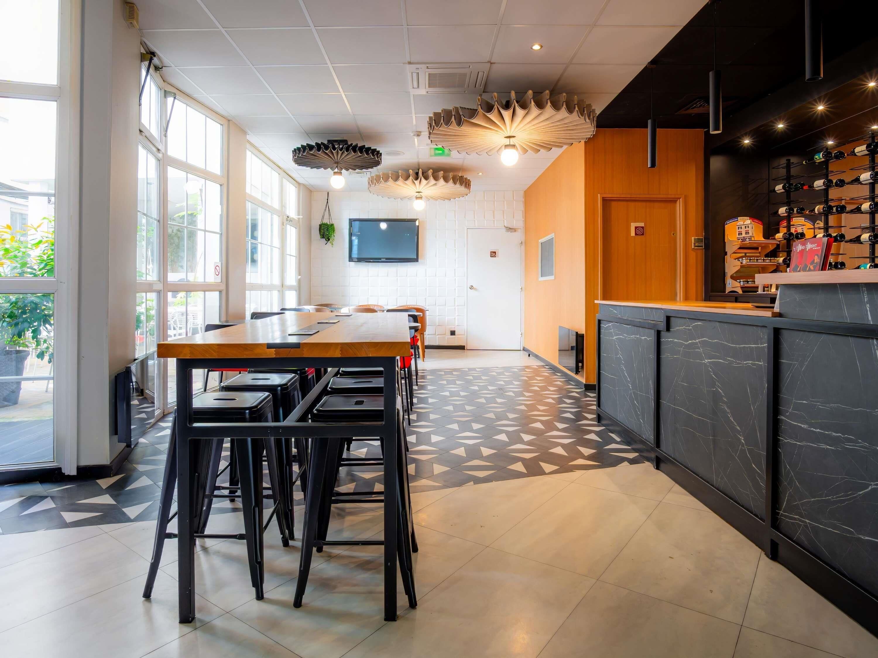 Un intérieur moderne avec une table et des chaises en bois, un sol à motifs et un coin bar avec des bouteilles de vin.
