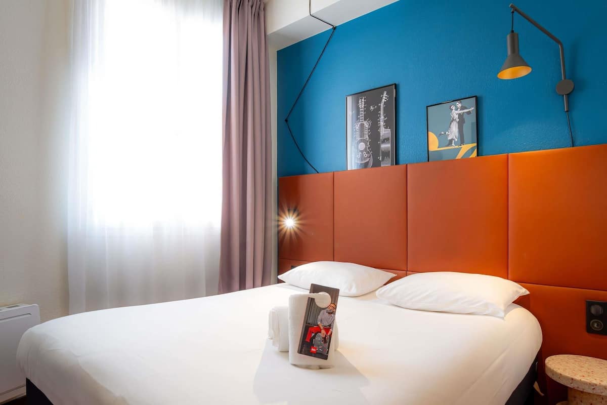 Ein Hotelzimmer mit Bett, Nachttisch, Lampe und einem Kunstwerk an der Wand.