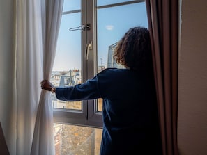 A person opening a window curtain in a room with a view of buildings outside. - ibis Paris Ornano Montmartre Nord 18ème (Paris)