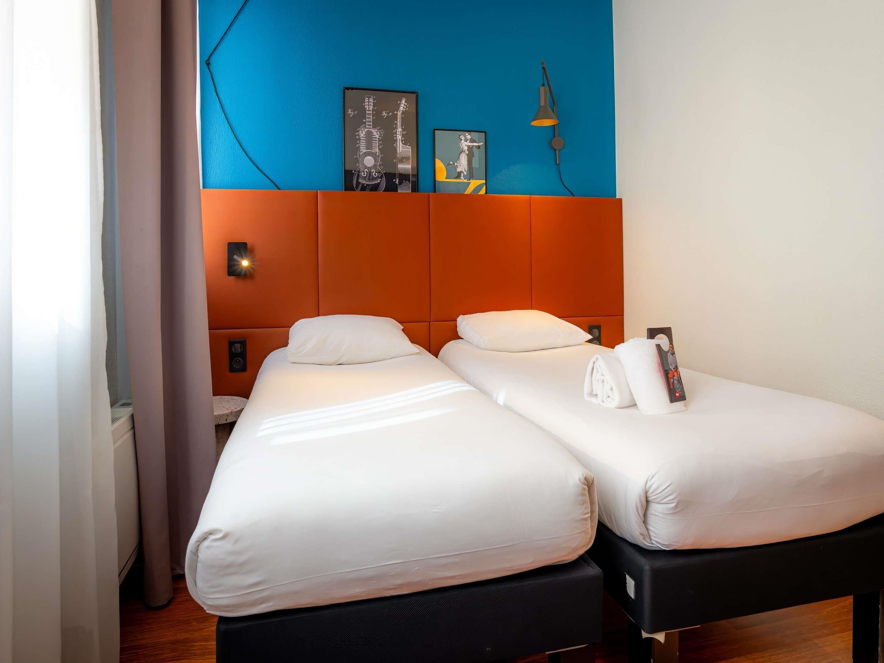 Habitación de hotel con dos camas, una pared de acento azul y una lámpara moderna.