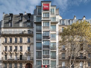 A multi-story hotel with a prominent 'ibis' sign, balconies with wrought iron railings, and a tree in the foreground. - ibis Paris Ornano Montmartre Nord 18ème (Paris)