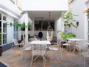 A patio area with white metal chairs and tables, surrounded by potted plants and a hanging chair. - ibis Paris Ornano Montmartre Nord 18ème (Paris)