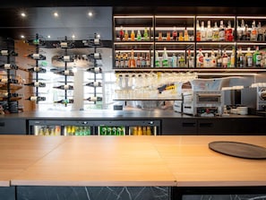 Uma área de bar com prateleiras de garrafas de bebidas, um espaço para vinhos e uma máquina de café.