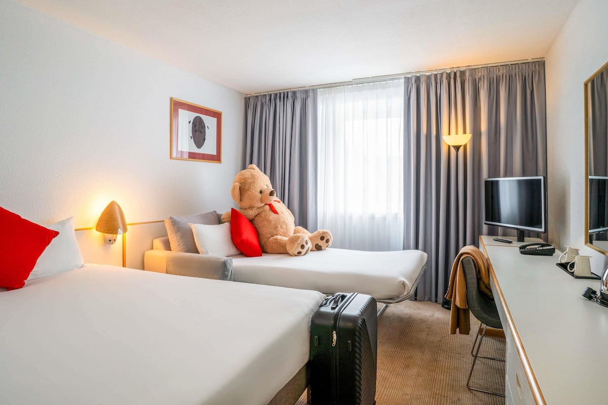Ein Hotelzimmer mit zwei Betten, einem Schreibtisch, einem Fernseher und einem großen Teddybären.