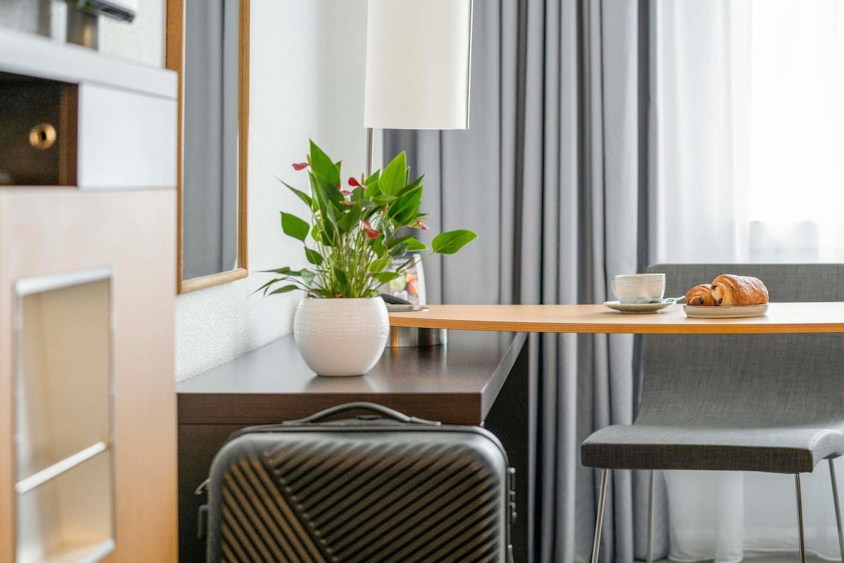 Ein modernes Hotelzimmer mit einem Holztisch, einem Blumentopf, einem Croissant und einer Tasse.