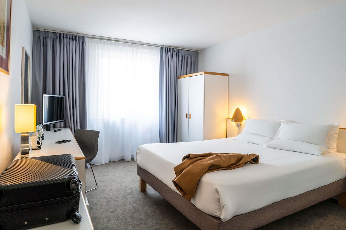 Ein Hotelzimmer mit Bett, Schreibtisch mit Computer, Stuhl, Koffer und Kleiderschrank.