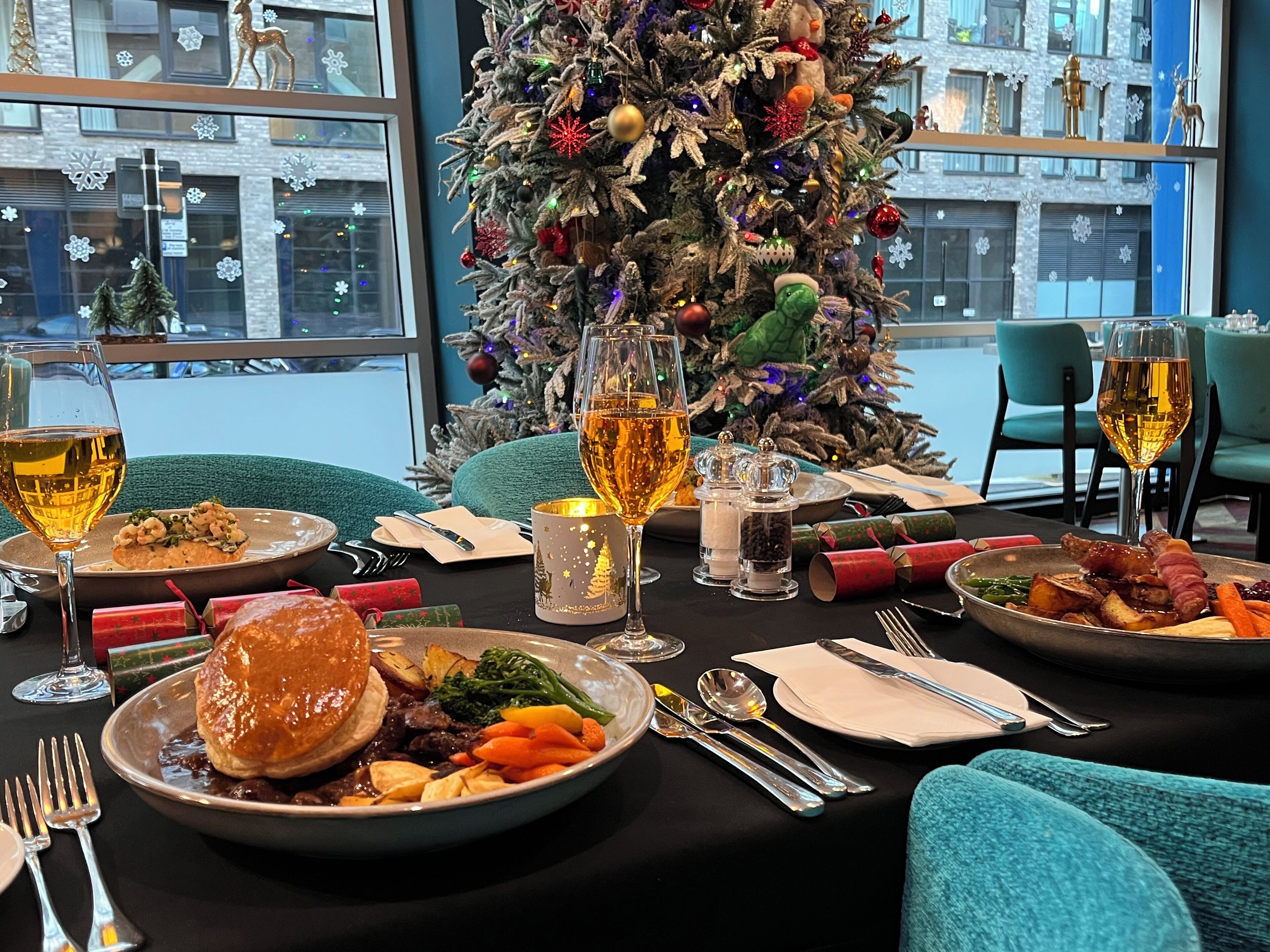 Een gedekte eettafel met borden eten, glazen wijn en kerstdecoraties.