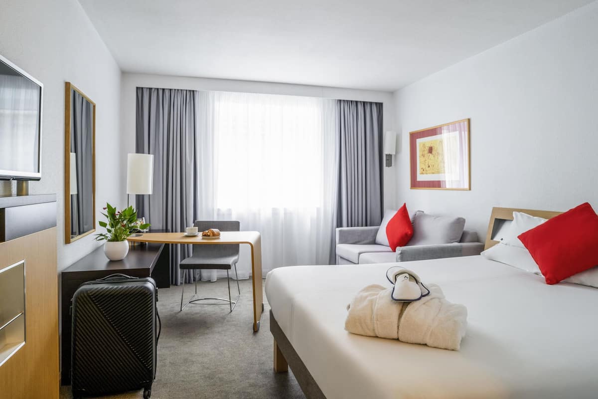 Ein Hotelzimmer mit Bett, Schreibtisch, Stuhl, Fernseher und einem Fenster mit Vorhängen.