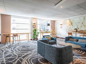 Un vestíbulo de hotel con bar, zona de estar y grandes ventanales.