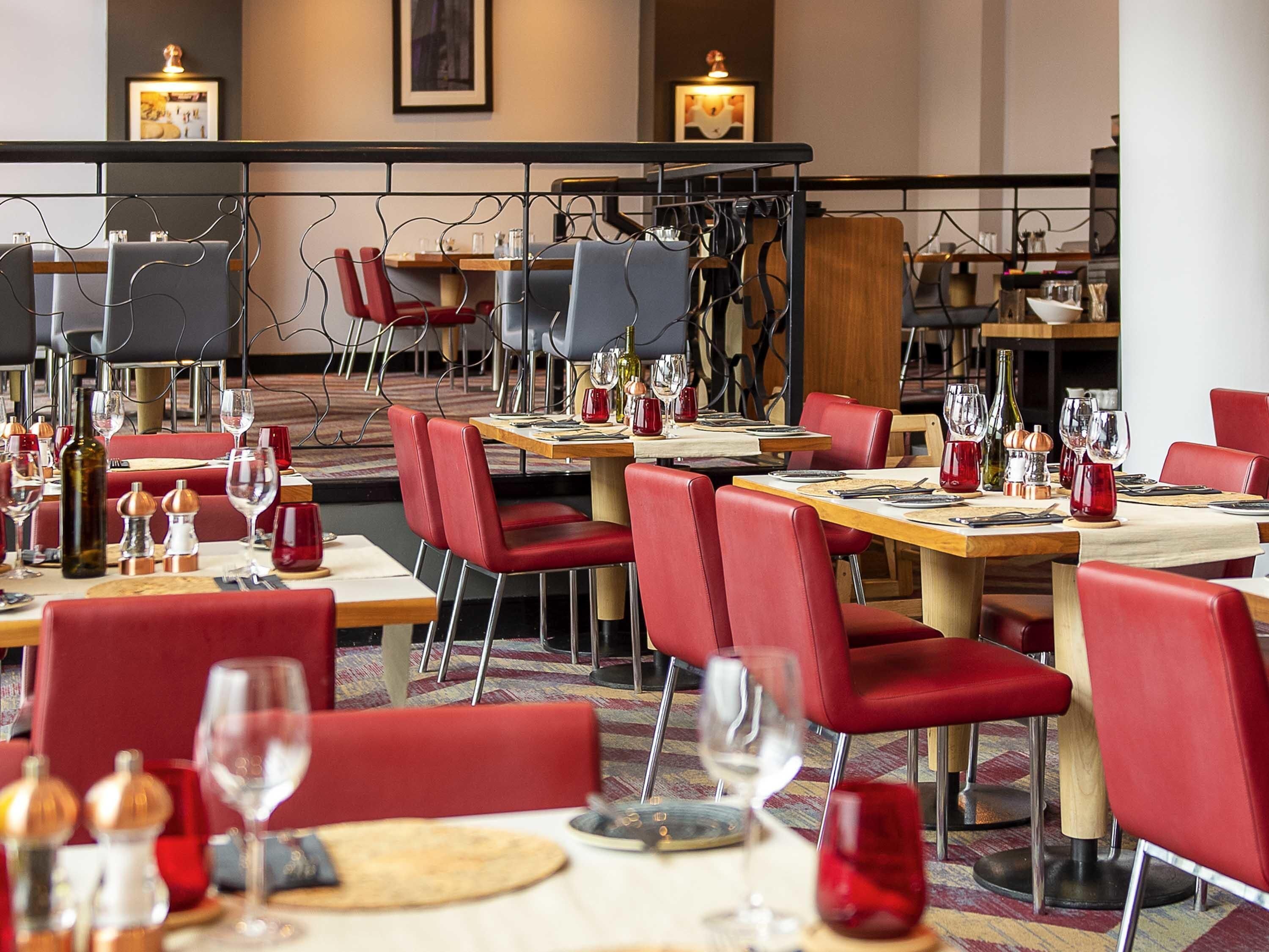A restaurant with red chairs, wooden tables, and wine glasses.