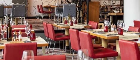 A restaurant with red chairs, wooden tables, and wine glasses.