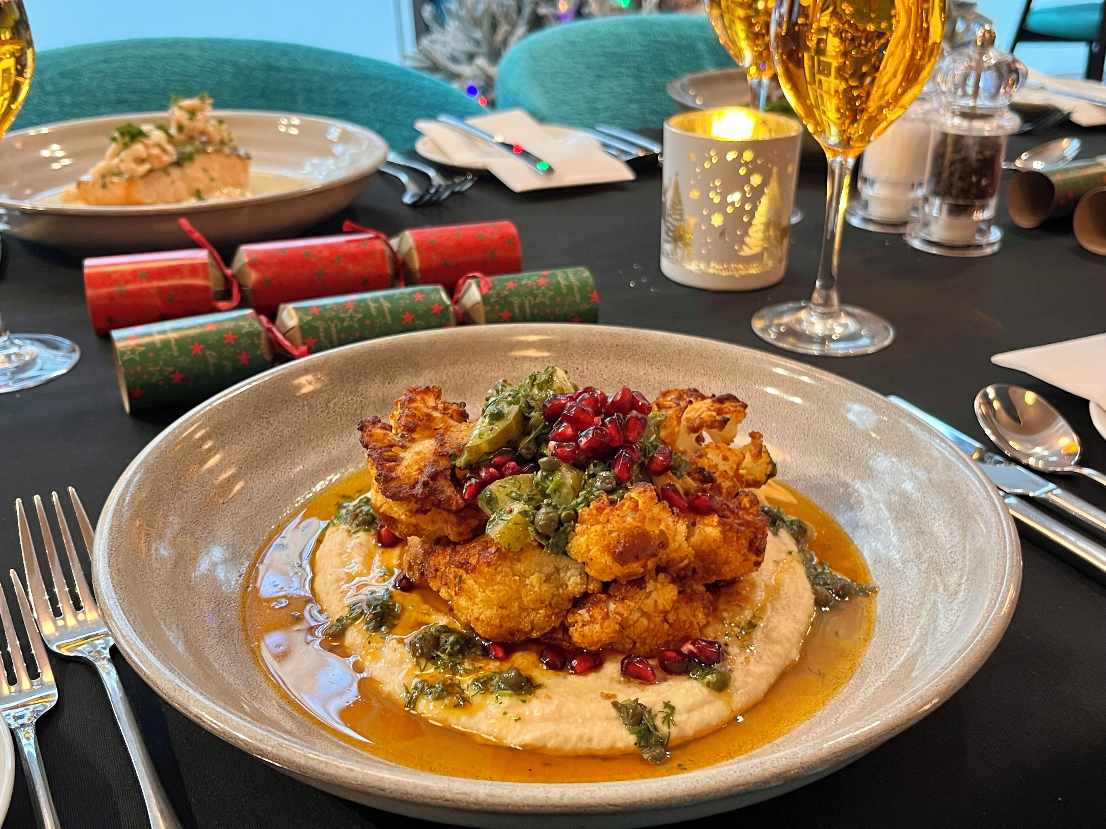 A plate of food with pomegranate and greens, a glass of wine, and Christmas decorations on a table.