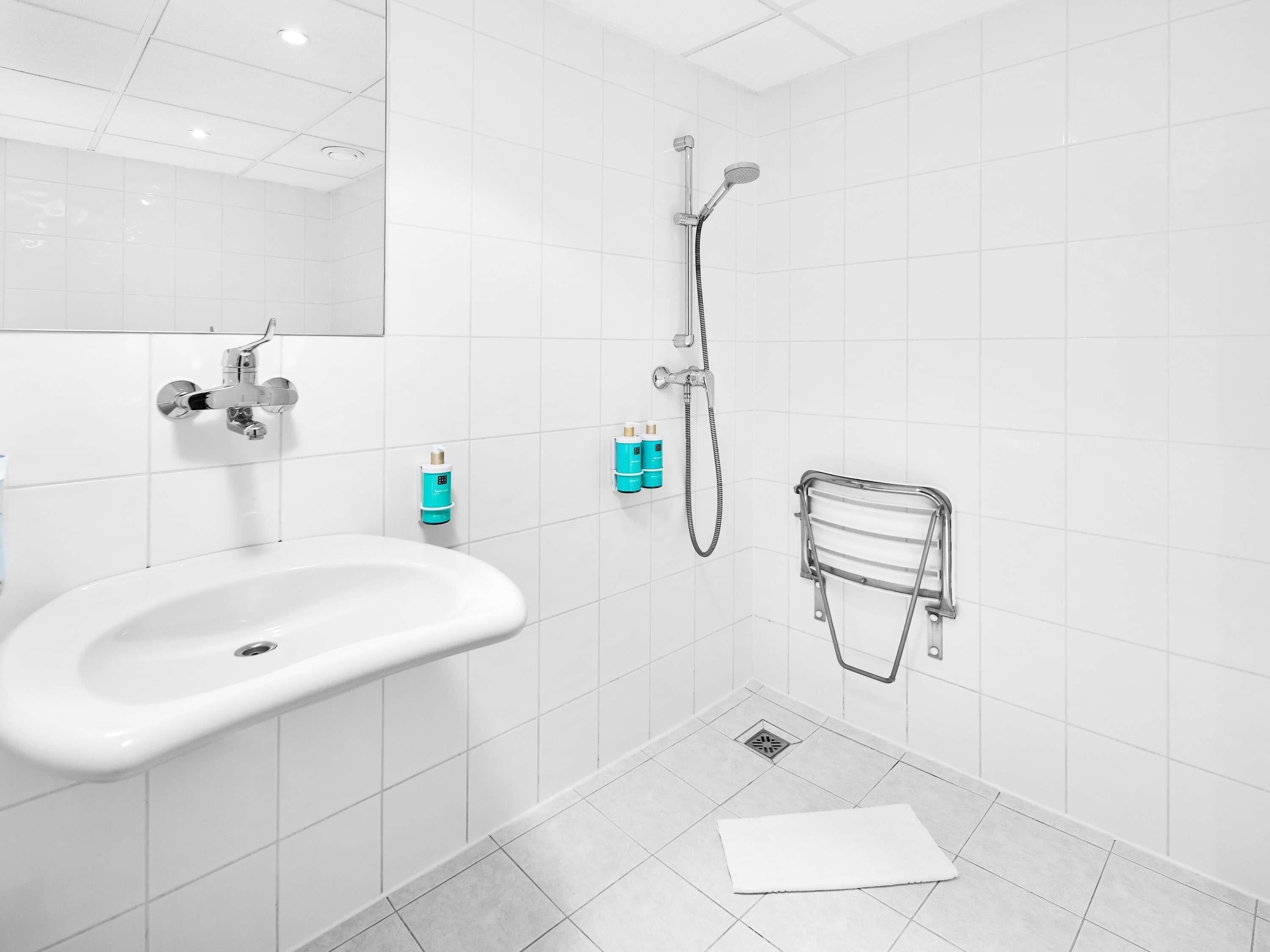 A modern bathroom with a white sink, a handheld showerhead, and a towel rack.