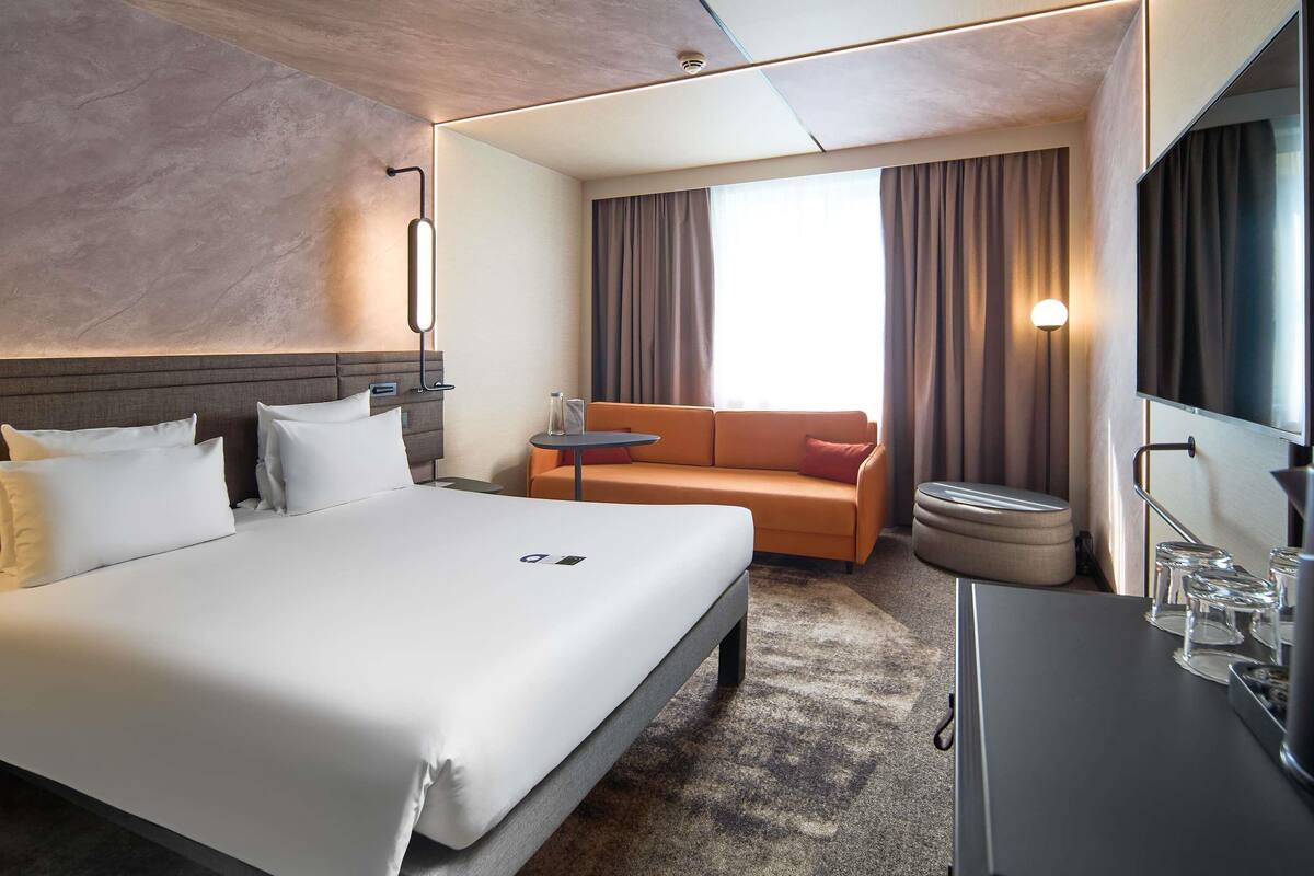 Une chambre d’hôtel comprenant un grand lit, un canapé, une petite table, une télévision et une salle de bain.