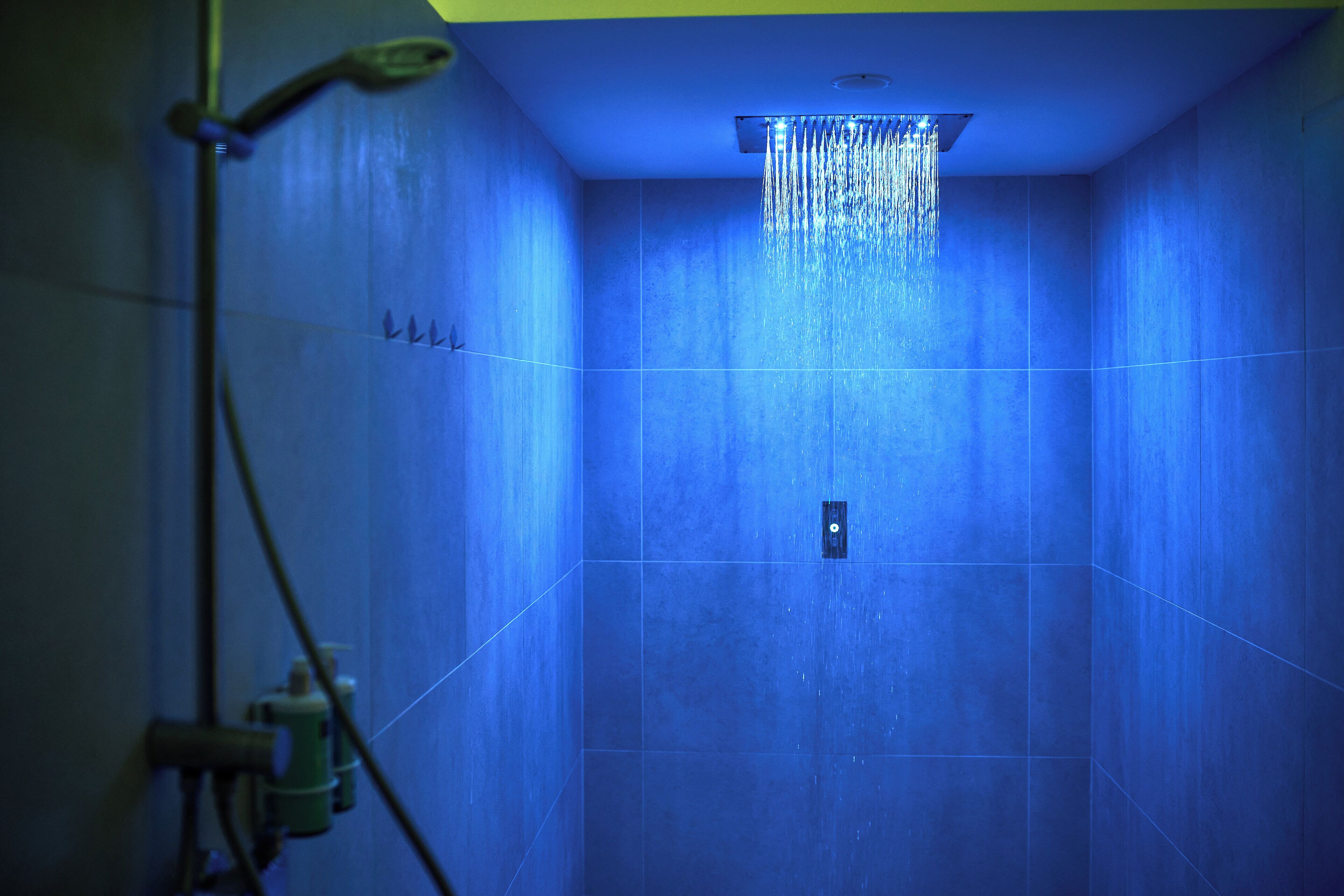 Un baño con paredes de azulejos azules, un cabezal de ducha y una tubería de agua a la vista.